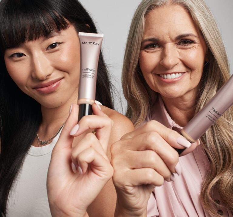 Two women smiling and each holding a tube of TimeWise 3D&reg; Foundation, showcasing buildable, true-to-skin coverage in different shades.